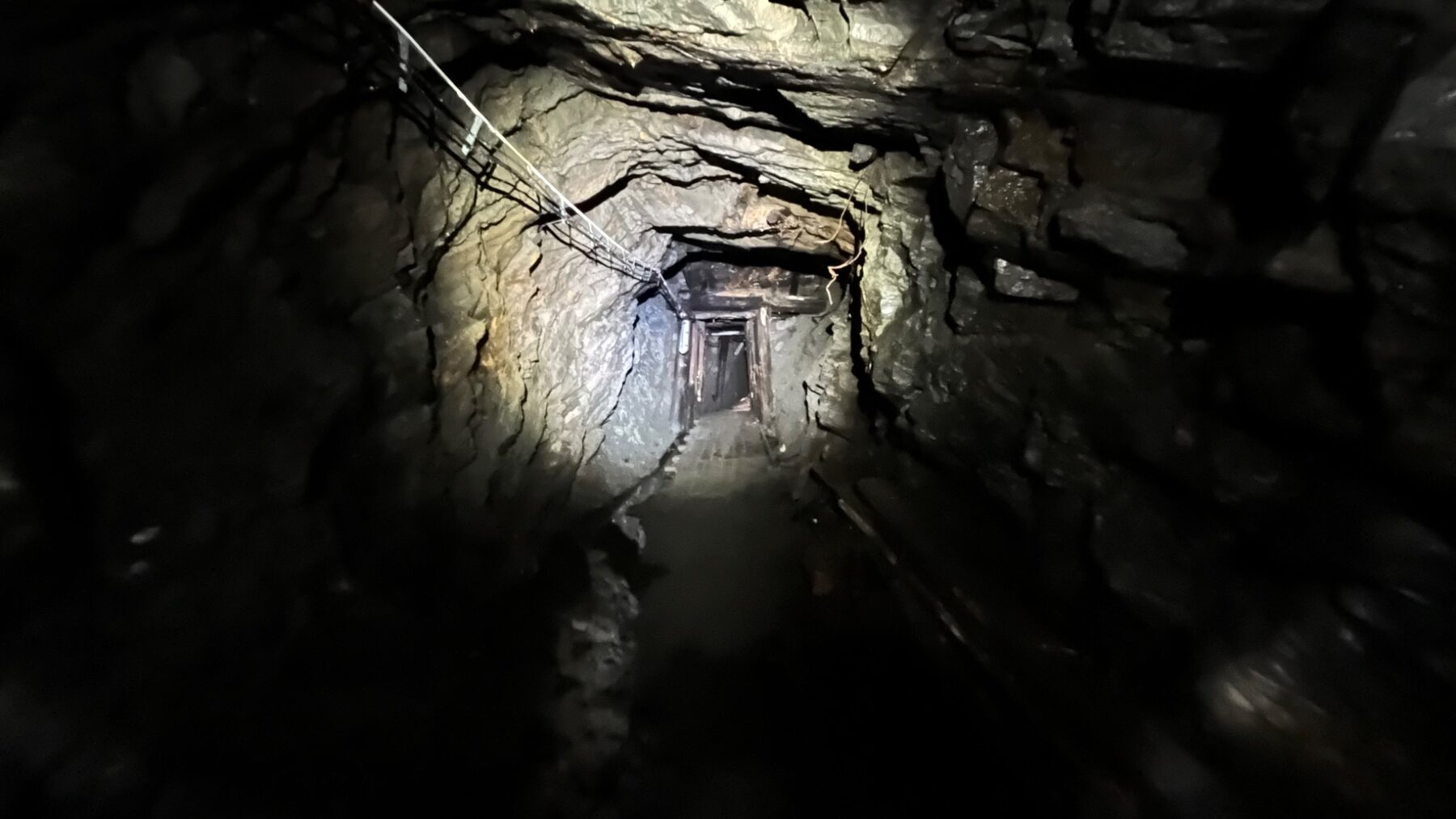Částečně zatopená důlní chodba osvětlená potápěčským světlem