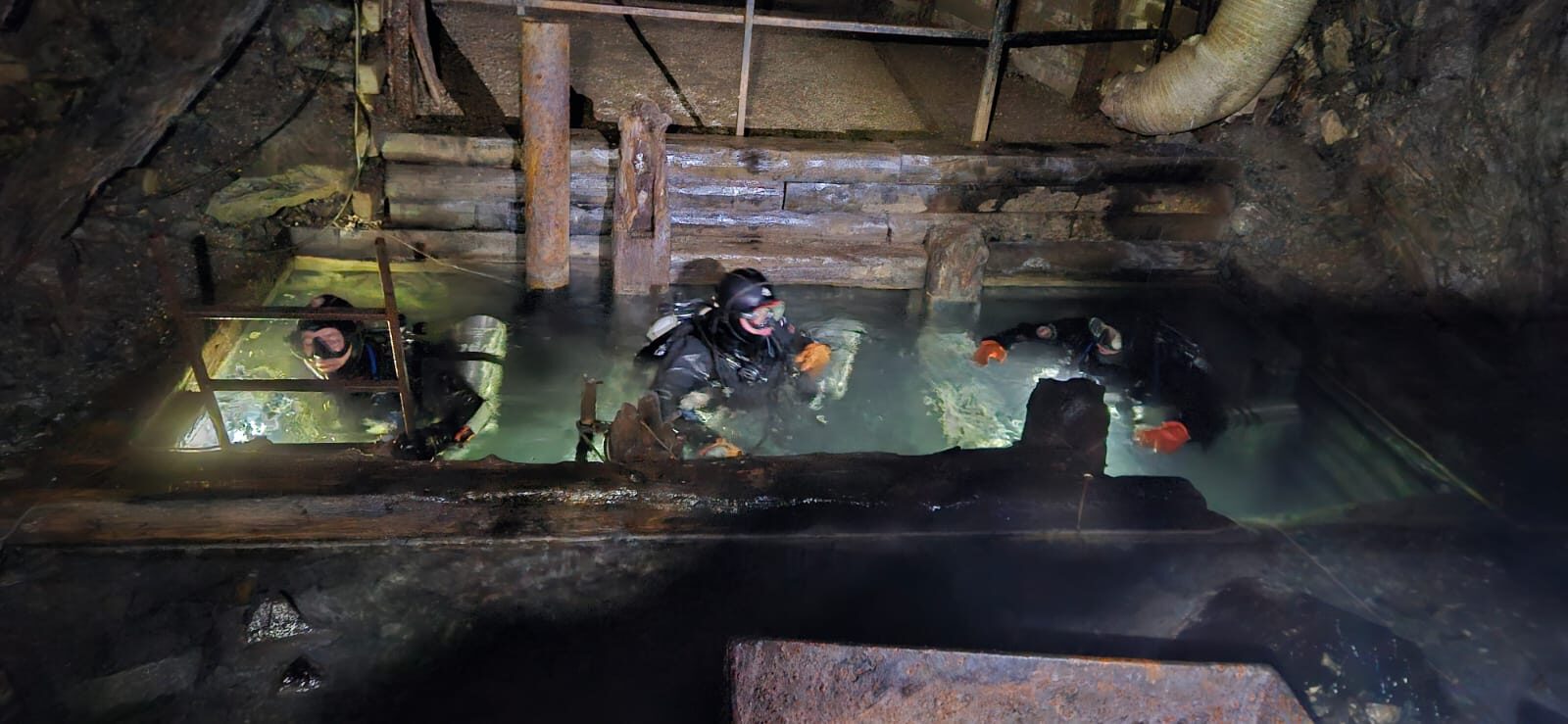 Potápěči ve vodě pod dřevěnou důlní konstrukcí